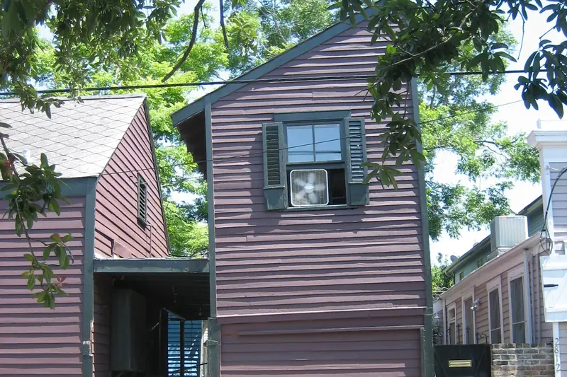 Tall, narrow clapboard house with a square box fan wedged into one of its second-floor windows